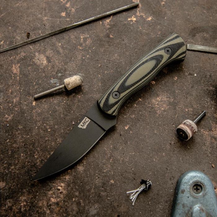 Montana Knife Company - The Blackfoot Fixed Blade 2.0 - Green and Black - Knife laying on work bench next to small, percision tools