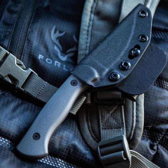 Montana Knife Company - The Blackfoot Fixed Blade 2.0 - Grey - knife inside black kydex sheath attached to a backpack strap, worn by a person in an outdoor, water resistant and ripstop technical jacket