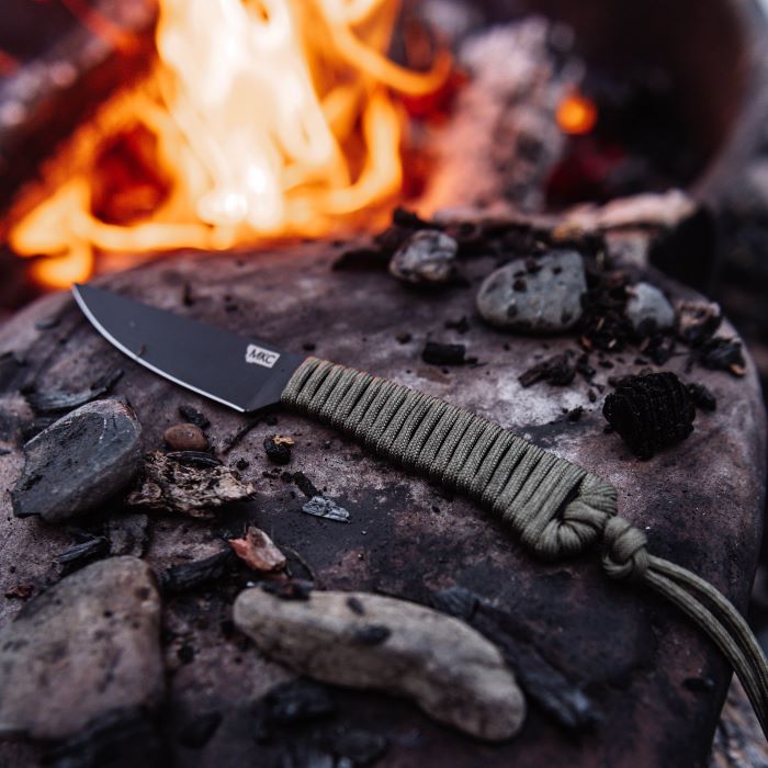 Montana Knife Company - The Speedgoat Fixed Blade - Olive - Knife laying on rock in front of fire next to small stones and charred wood pieces